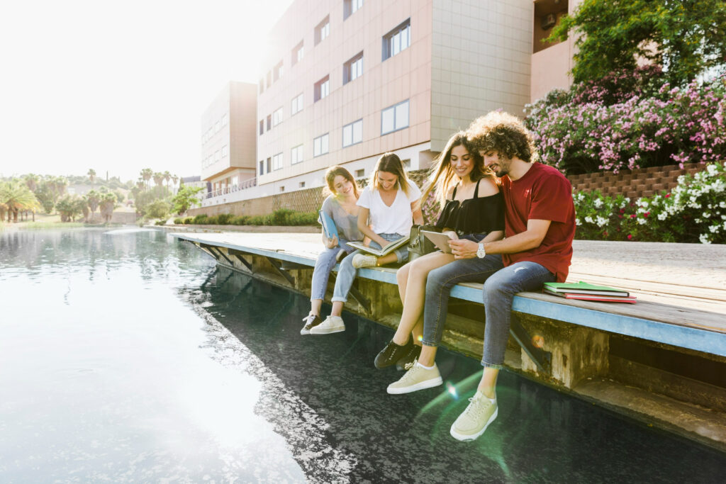 university friends studying near building with lake